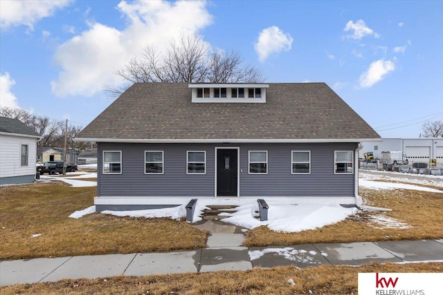 view of front facade with a shingled roof and a front lawn