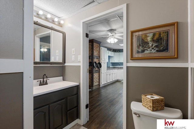 bathroom with toilet, ceiling fan, a textured ceiling, vanity, and wood finished floors