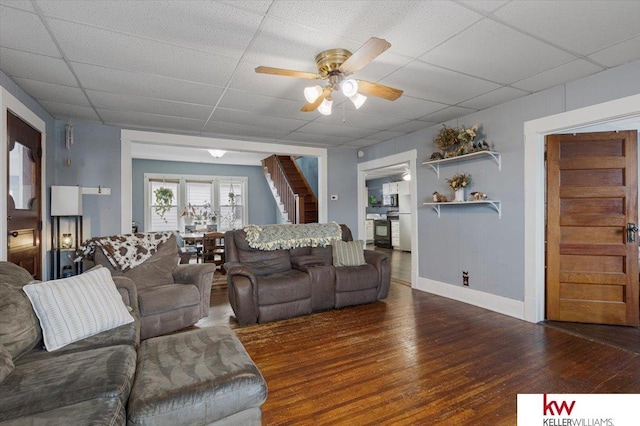 living room with baseboards, a ceiling fan, a drop ceiling, wood finished floors, and stairs