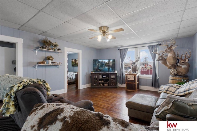 living area featuring ceiling fan, wood finished floors, a paneled ceiling, and baseboards