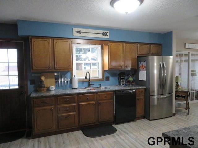 kitchen featuring black dishwasher, light wood-style floors, freestanding refrigerator, a sink, and a textured ceiling