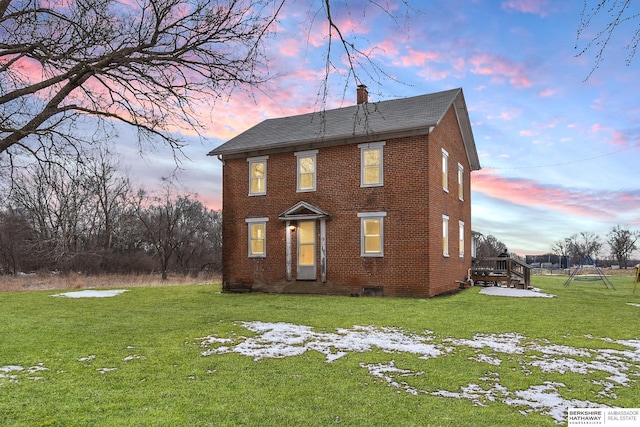 back of property at dusk featuring crawl space, brick siding, a yard, and a chimney