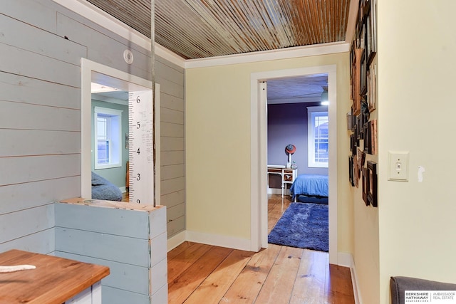 corridor with light wood-type flooring, wood ceiling, wood walls, and baseboards