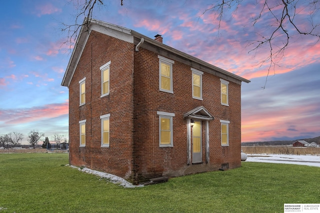 property exterior at dusk with a yard, a chimney, and brick siding