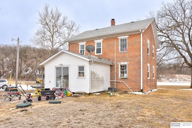 back of house featuring brick siding, a lawn, and a chimney