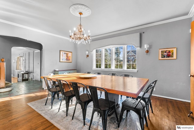 dining space featuring baseboards, arched walkways, crown molding, and wood finished floors