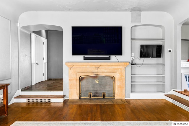 unfurnished living room with built in shelves, visible vents, and wood finished floors