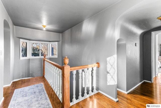 hallway featuring arched walkways, wood finished floors, an upstairs landing, and baseboards