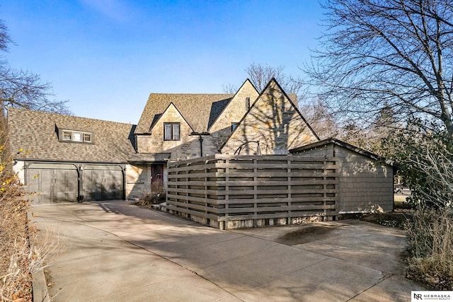 view of front of home with concrete driveway, a shingled roof, an attached garage, and fence