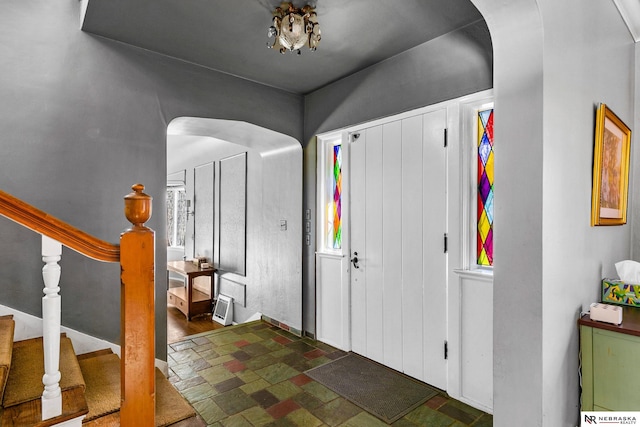 foyer featuring arched walkways, stone finish flooring, and stairs