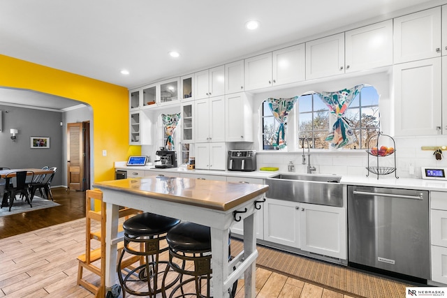 kitchen with light wood finished floors, white cabinets, backsplash, stainless steel dishwasher, and a sink