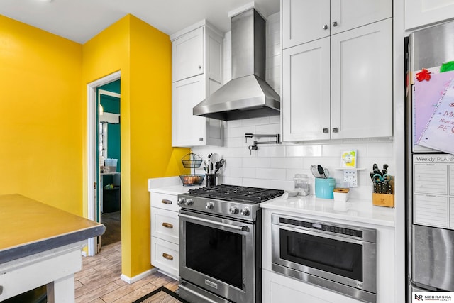 kitchen featuring white cabinetry, light countertops, appliances with stainless steel finishes, wall chimney range hood, and decorative backsplash