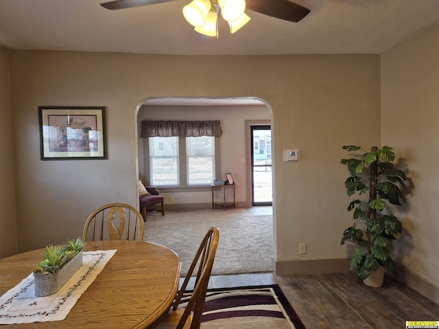 carpeted dining room with baseboards, arched walkways, and a ceiling fan