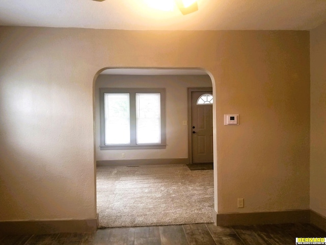 foyer with arched walkways, wood finished floors, and baseboards