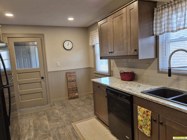 kitchen featuring a wealth of natural light, a wainscoted wall, a sink, and black appliances