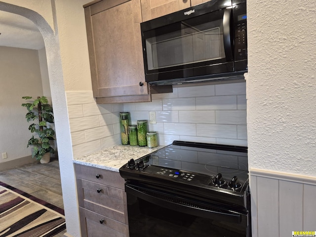 kitchen with arched walkways, a textured wall, wainscoting, black appliances, and backsplash