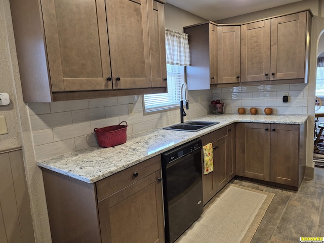 kitchen with black dishwasher, a sink, backsplash, and light wood finished floors