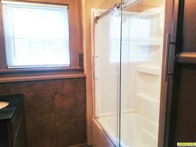 full bath with tile walls, vanity, and bath / shower combo with glass door