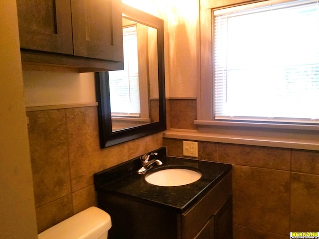 bathroom featuring wainscoting, vanity, toilet, and tile walls