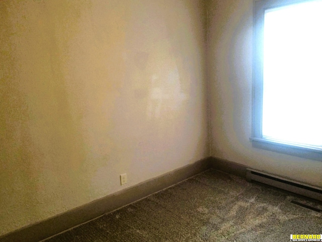 carpeted empty room featuring a baseboard heating unit and baseboards