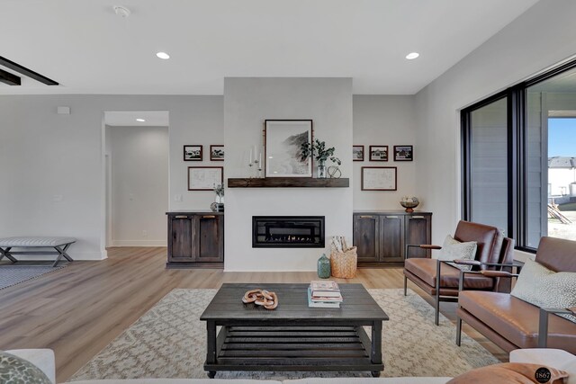 living room with baseboards, light wood finished floors, a glass covered fireplace, and recessed lighting