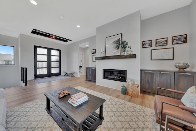 living area with recessed lighting, light wood-style flooring, a glass covered fireplace, and french doors