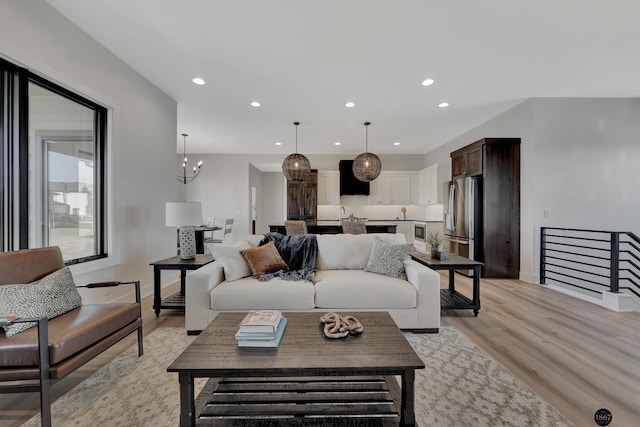 living room featuring baseboards, light wood-type flooring, an inviting chandelier, and recessed lighting