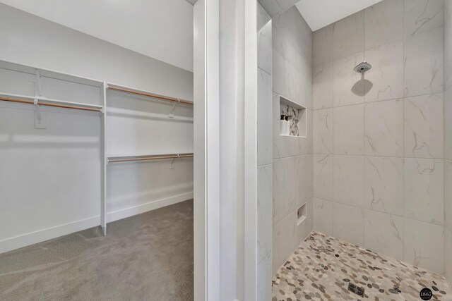 full bath featuring a spacious closet, a tile shower, and baseboards