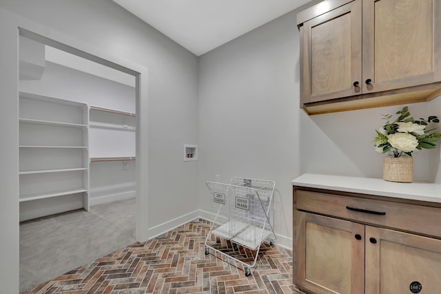 clothes washing area featuring cabinet space, baseboards, washer hookup, and brick floor