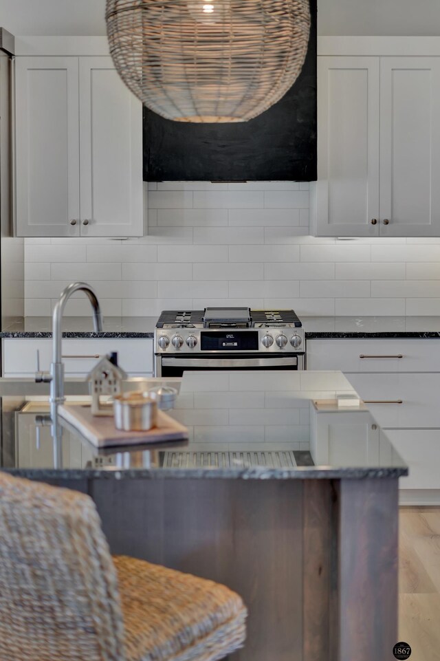 kitchen featuring backsplash, stainless steel range with gas stovetop, a sink, white cabinetry, and dark stone countertops