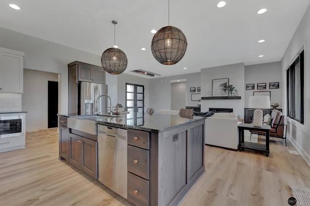 kitchen featuring stainless steel appliances, light wood-style floors, a sink, and dark stone countertops