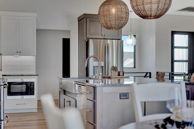 kitchen with hanging light fixtures, backsplash, freestanding refrigerator, light wood finished floors, and a center island with sink