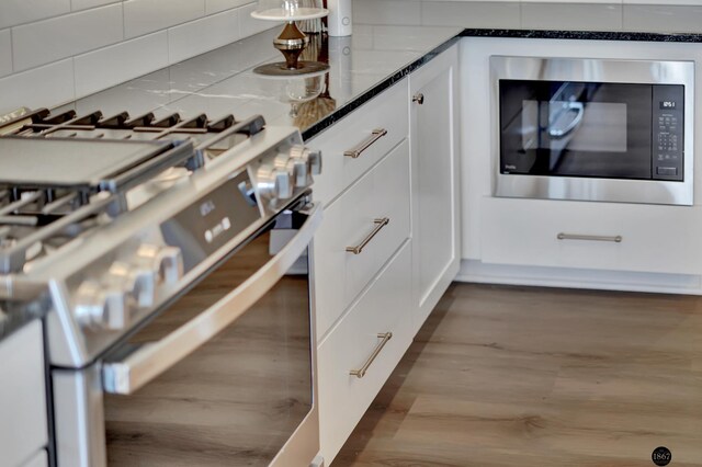 room details with stainless steel range with gas cooktop, dark wood finished floors, tasteful backsplash, white cabinetry, and built in microwave