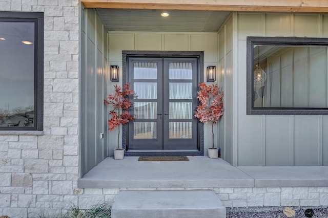 view of exterior entry with stone siding, french doors, and board and batten siding