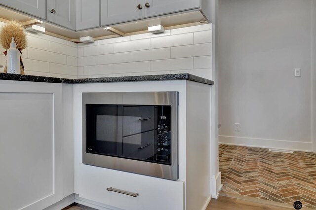 interior details featuring dark stone counters, stainless steel microwave, and baseboards