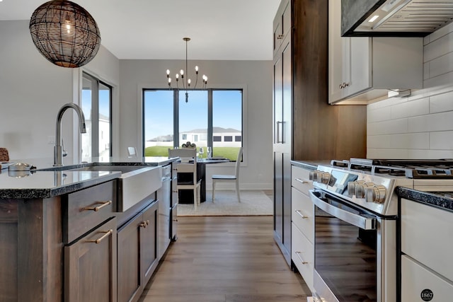 kitchen with a notable chandelier, decorative backsplash, wood finished floors, stainless steel gas range, and wall chimney exhaust hood