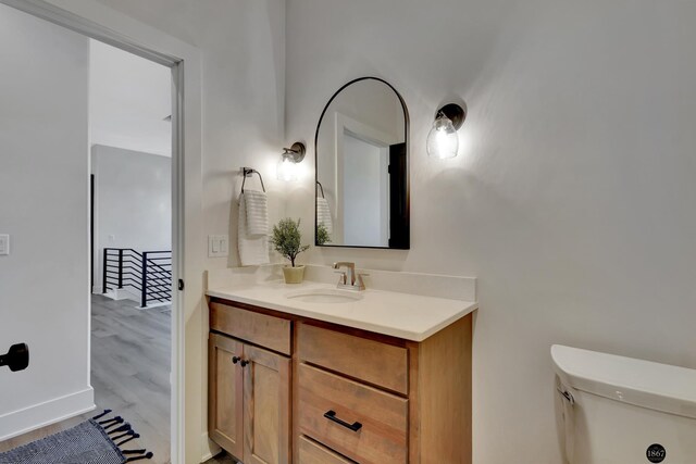 half bath with toilet, wood finished floors, vanity, and baseboards