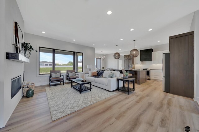 living room featuring light wood-style flooring, recessed lighting, baseboards, a glass covered fireplace, and an inviting chandelier