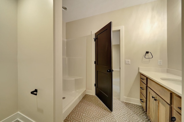 bathroom featuring tile patterned flooring, baseboards, walk in shower, and vanity