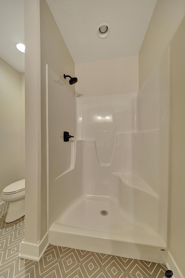 bathroom featuring toilet, tile patterned flooring, baseboards, and walk in shower