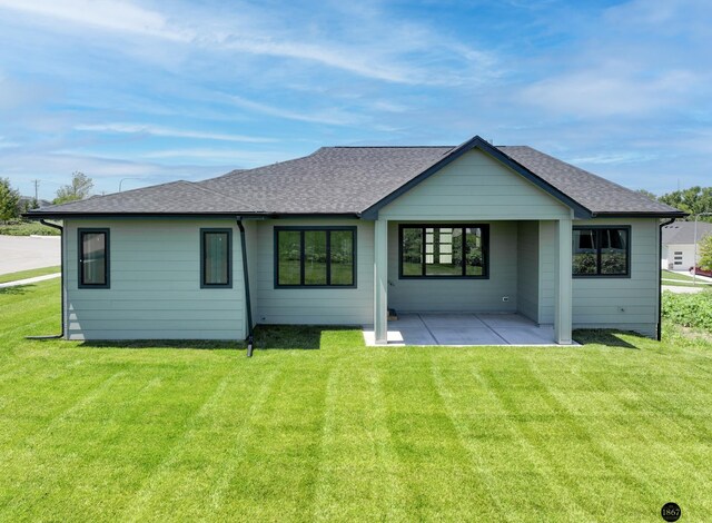 back of house with a patio area, roof with shingles, and a lawn