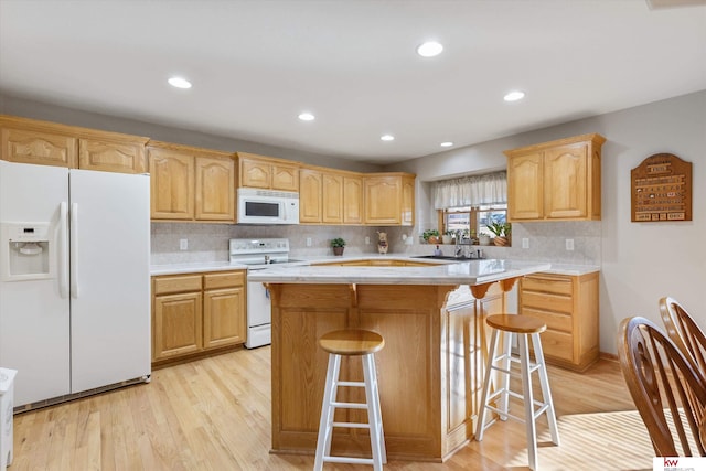 kitchen with light brown cabinets, white appliances, a kitchen island, light wood-style floors, and light countertops