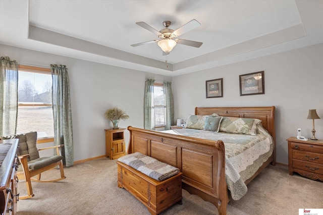 bedroom with light carpet, baseboards, a tray ceiling, and a ceiling fan