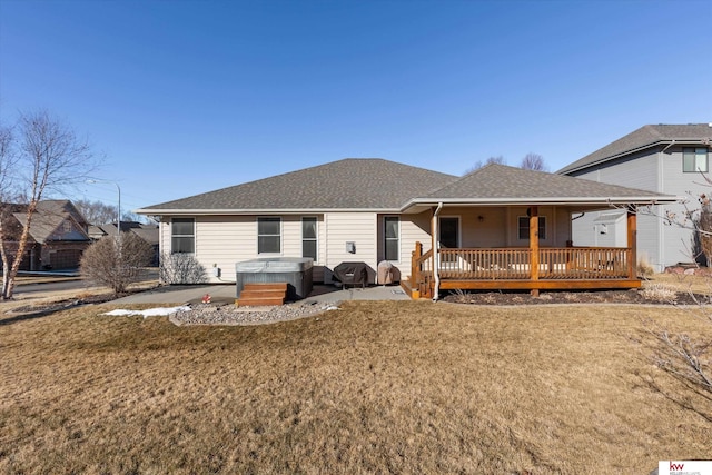 rear view of house featuring roof with shingles, a yard, a hot tub, and a patio