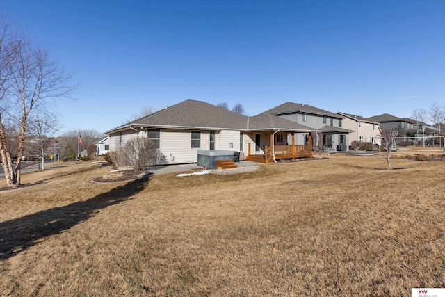 rear view of property with a hot tub, a shingled roof, a lawn, and a wooden deck