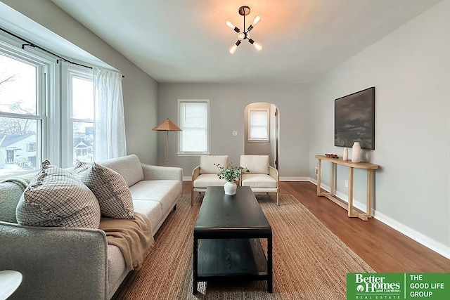 living room with arched walkways, an inviting chandelier, baseboards, and wood finished floors