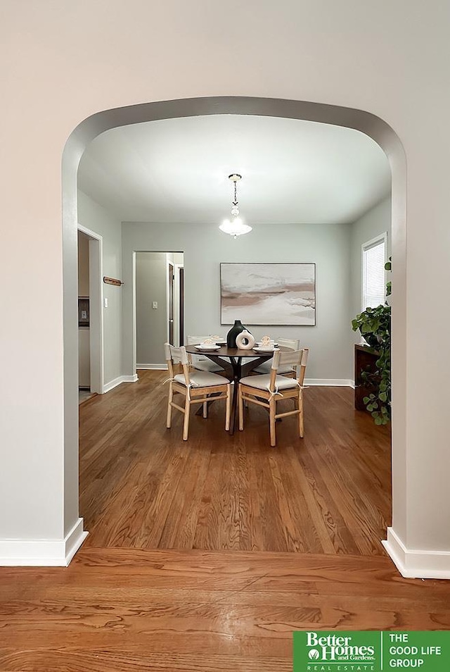 dining space with arched walkways, baseboards, and wood finished floors