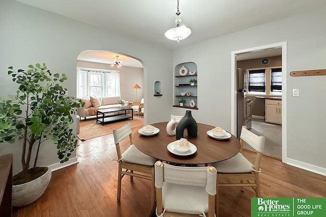 dining area with light wood-type flooring, arched walkways, baseboards, and built in shelves