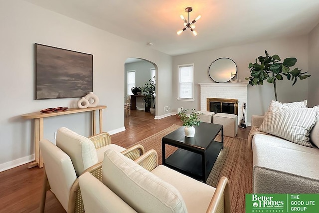 living area featuring arched walkways, a fireplace, baseboards, and wood finished floors