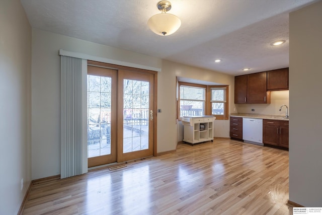 kitchen featuring light wood finished floors, light countertops, a sink, a textured ceiling, and dishwasher